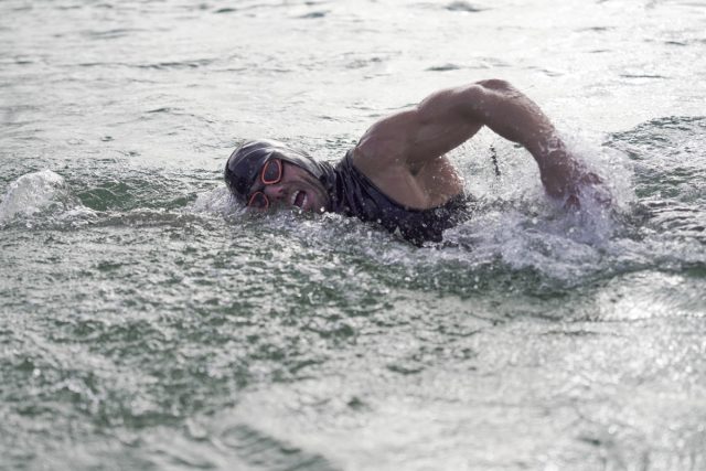 well muscled man in torso swim suit and swim cap swimming in open water