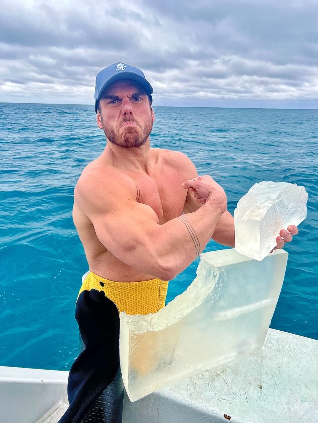 well muscled man in blue baseball cap flexes his bicep next to gelatin cube with a shark bite taken out of it