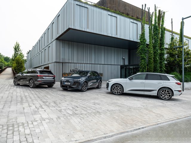 Three Audi Q6 e-trons outside a modern wood-clad building