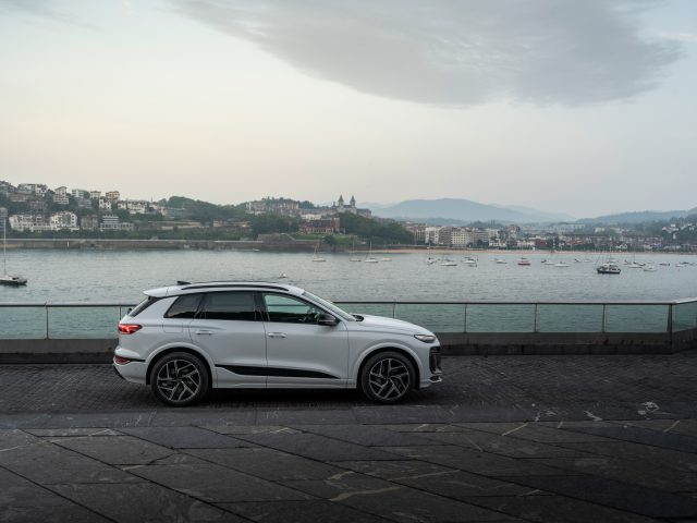 A white Audi Q6 e-tron in profile, by the sea