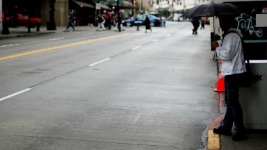 a person on a sidewalk in downtown Seattle, preparing to jaywalk across the street."