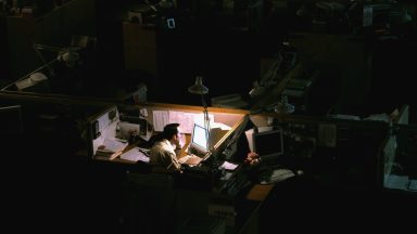 Man works late in dimly lit cubicle amid a dark office space