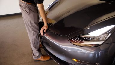 An employee closes the front hood of a Tesla Inc. Model 3 electric vehicle at the company's showroom in Newport Beach, California, U.S., on Friday, July 6, 2018.