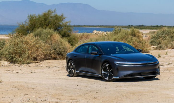 A Lucid Air parked on some sand in front of a lake with mountains in the distance