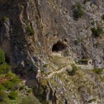 Image of a sheer cliff face with a narrow path leading to a cave opening.