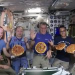 Image of astronauts aboard the ISS showing off pizzas they've made.