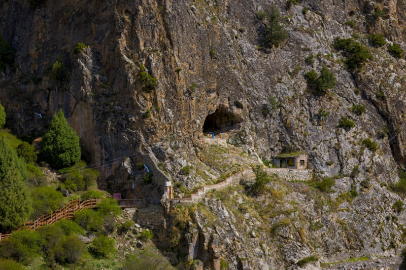 Image of a sheer cliff face with a narrow path leading to a cave opening.