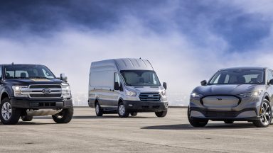 A ford F-150 Lightning, E-Transit, and Mustang Mach-E parked in a row