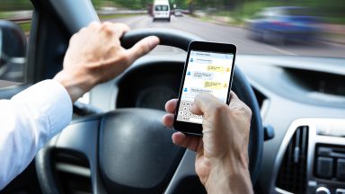 Close-up Of A Man's Hand Typing Text Message On Mobile Phone While Driving Car