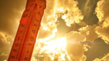 A warm orange sun partly obscured by clouds, with a distorted, melting thermometer in the foreground.