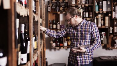 Man looking over the offerings at a wine store with a tablet in hand.