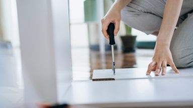 Cropped shot of young woman assembling furniture with a screwdriver. She is assembling a wooden cabinet in the living room in her new apartment