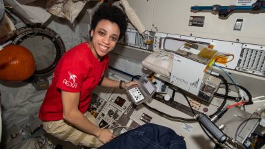 I woman holds a handheld device in front of a rack of equipment.