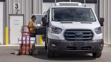 A woman loads things into the side of a Ford E-Transit that's been uplifted as a refrigerated van