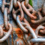 Rusty links of a chain, against an also-rusted metal background.