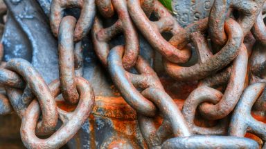 Rusty links of a chain, against an also-rusted metal background.