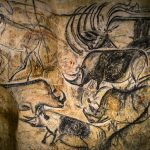 Image of a tan rock surface with black and brown depictions of animals on it.