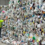 A man stands next to piles of compressed plastic bottles.