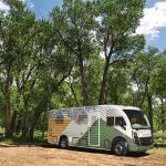 A white, green, and yellow RV parked next to some trees