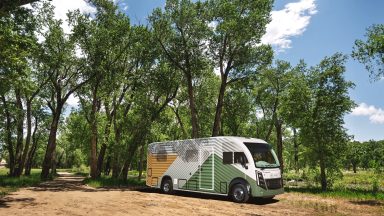 A white, green, and yellow RV parked next to some trees