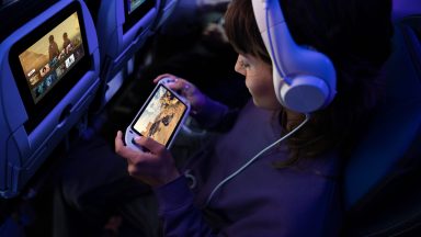 A child plays with a handheld games console while sitting in an airplane seat