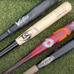 four different kinds of wood and metal bats laid flat on baseball diamond grass