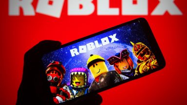 Someone holding up a smartphone with "Roblox" on the screen.