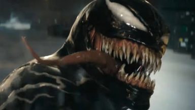 closeup of alien symbiote Venom facing camera with long tonge lolling out of a mouth lined with sharp teeth