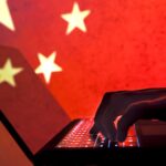 A person typing on a laptop with a Chinese flag in the background