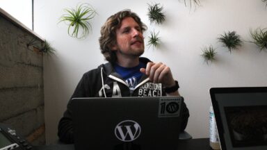 Matt Mullenweg of WordPress company Automattic sits in front of a laptop adorned with a WordPress logo.