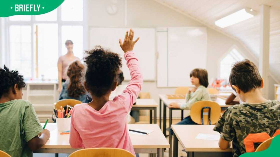 A young learner raising her hand to answer a question in class