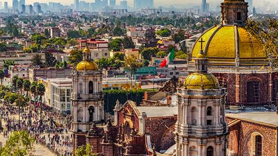 Mexico. Basilica of Our Lady of Guadalupe. Cupolas of the old basilica and cityscape of Mexico City on the far