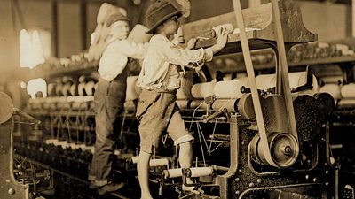 Young boys working in a thread spinning mill in Macon, Georgia, 1909. Boys are so small they have to climb onto the spinning frame to reach and fix broken threads and put back empty bobbins. Child labor. Industrial revolution