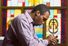 African American man praying in church with stained glass in background