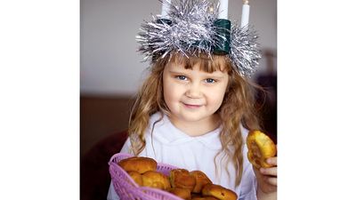 Saint Lucia Day. Young girl wears Lucia crown (tinsel halo) with candles. Holds Saint Lucia Day currant laced saffron buns (lussekatter or Lucia's cats). Observed December 13 honor virgin martyr Santa Lucia (St. Lucy). Luciadagen, Christmas, Sweden