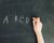 child's hand with chalk write letters a, b, c, d on black chalkboard