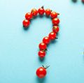 Red and yellow cherry tomatoes, some forming a question mark, against a light blue background. (organic, fruits, vegetables)