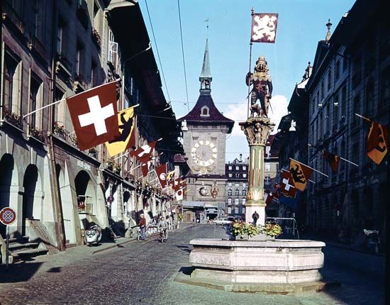 The medieval Clock Tower in Bern, Switzerland, seen from the Kramgasse. In the foreground is the Zähringen Fountain, surmounted by a bear in armour, the city's heraldic device.