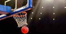 A ball swishes through the net at a basketball game in a professional arena.