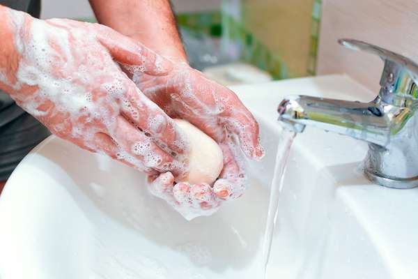 Man washing his hands with a bar of soap over a sink with water running. (hygiene, cleanliness, hand washing)