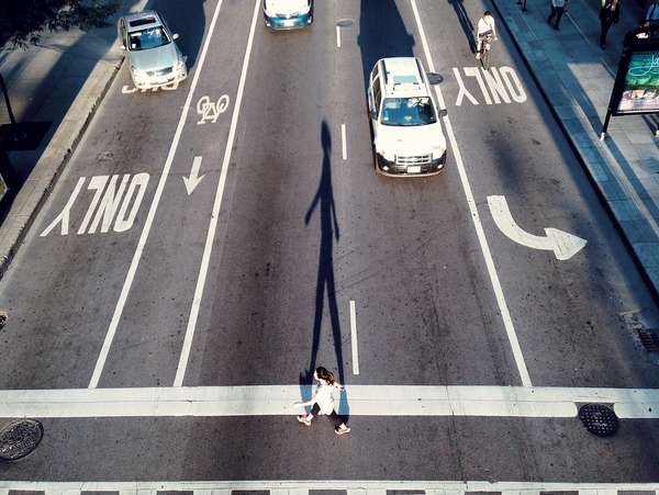 High angle view of a woman crossing a road. City streets, asphalt, bike lanes, car  traffic, pedestrians