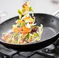 Chef tossing vegetables in a frying pan over a burner (skillet, food).