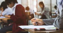 Close-up of hand of student holding a pen and taking an exam in a classroom (testing, tests, education).