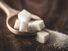 Zoomed in photo of a pile of sugar cubes in a wooden stop on a wooden table.