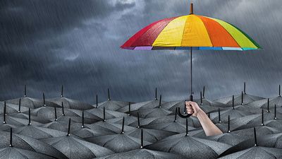 Umbrella colored like a rainbow sticking out above a sea of black umbrellas while it rains. (storm, weather)