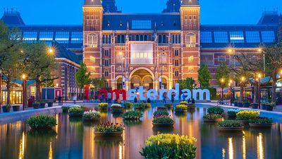 Rijksmuseum building famous landmark in Amsterdam. Blue hour dusk evening illumination with tulip flowers in vases in pools.