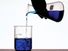 A person's hand pouring blue fluid from a flask into a beaker. Chemistry, scientific experiments, science experiments, science demonstrations, scientific demonstrations.