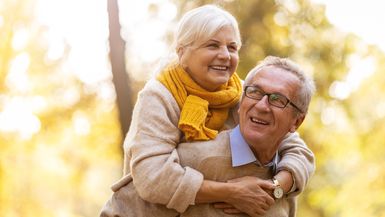 Photo of a senior man giving his wife a piggyback outdoors.