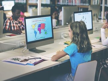 Grade school students working at computers in a school library. Study learn girl child class technology