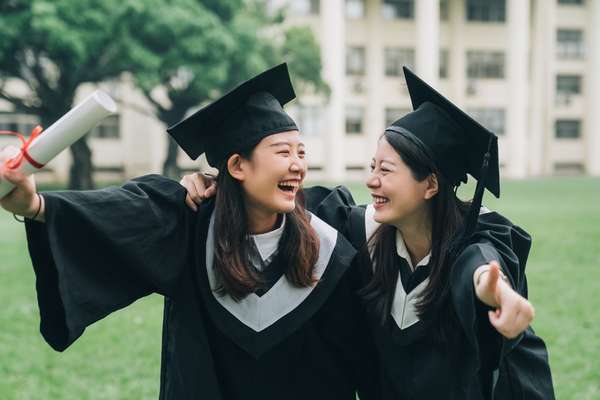 Graduation asian female friends hold diploma. cheerful students hugging shoulders arms with thumbs up beautiful cheerful women students looking each other smiling